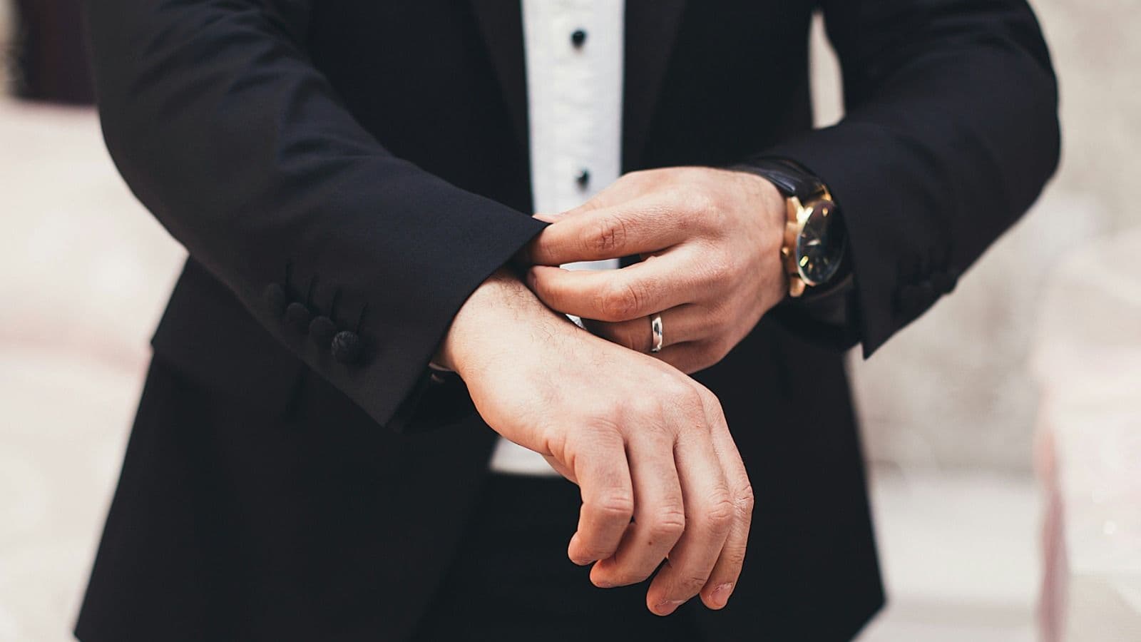 Close-up of a man adjusting the cuff of his black suit jacket, wearing a stylish watch and silver ring, symbolizing elegance, power, and peak masculinit